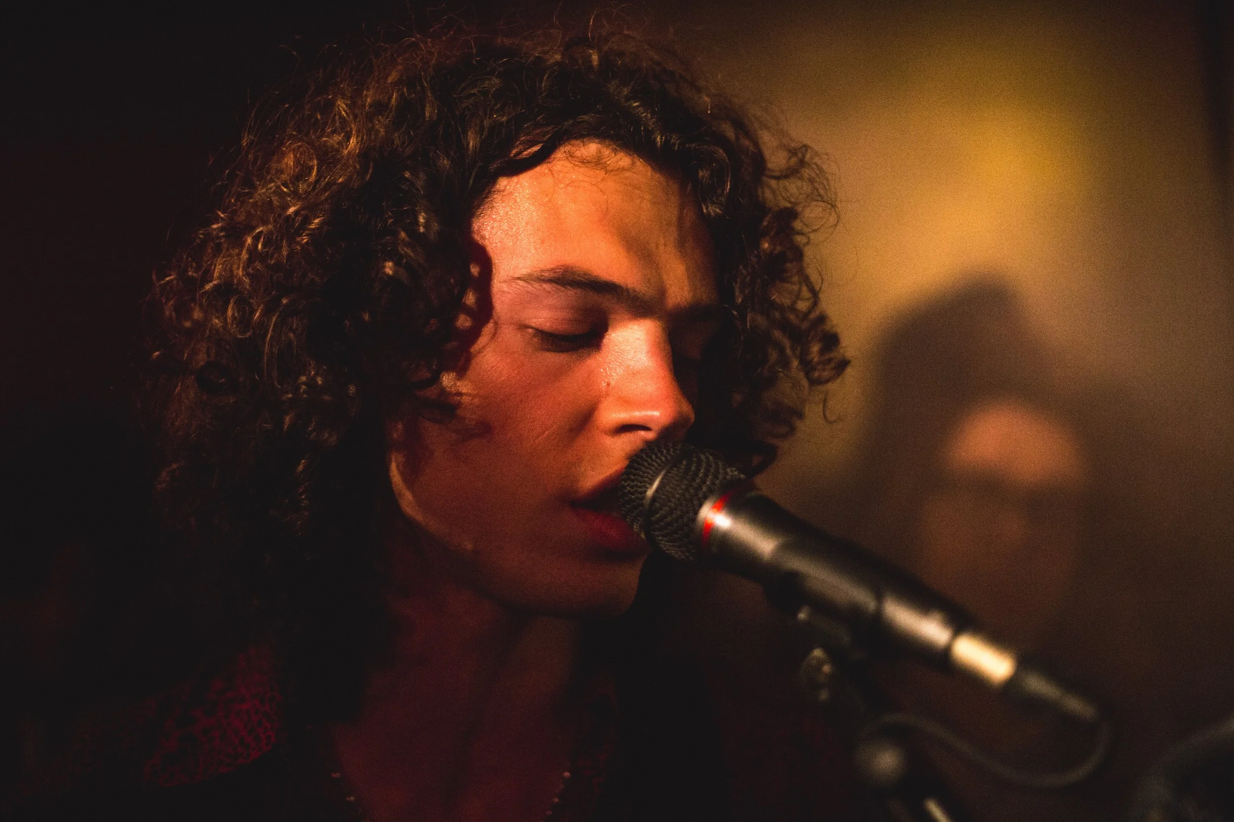 A woman with curly hair singing into a microphone.
