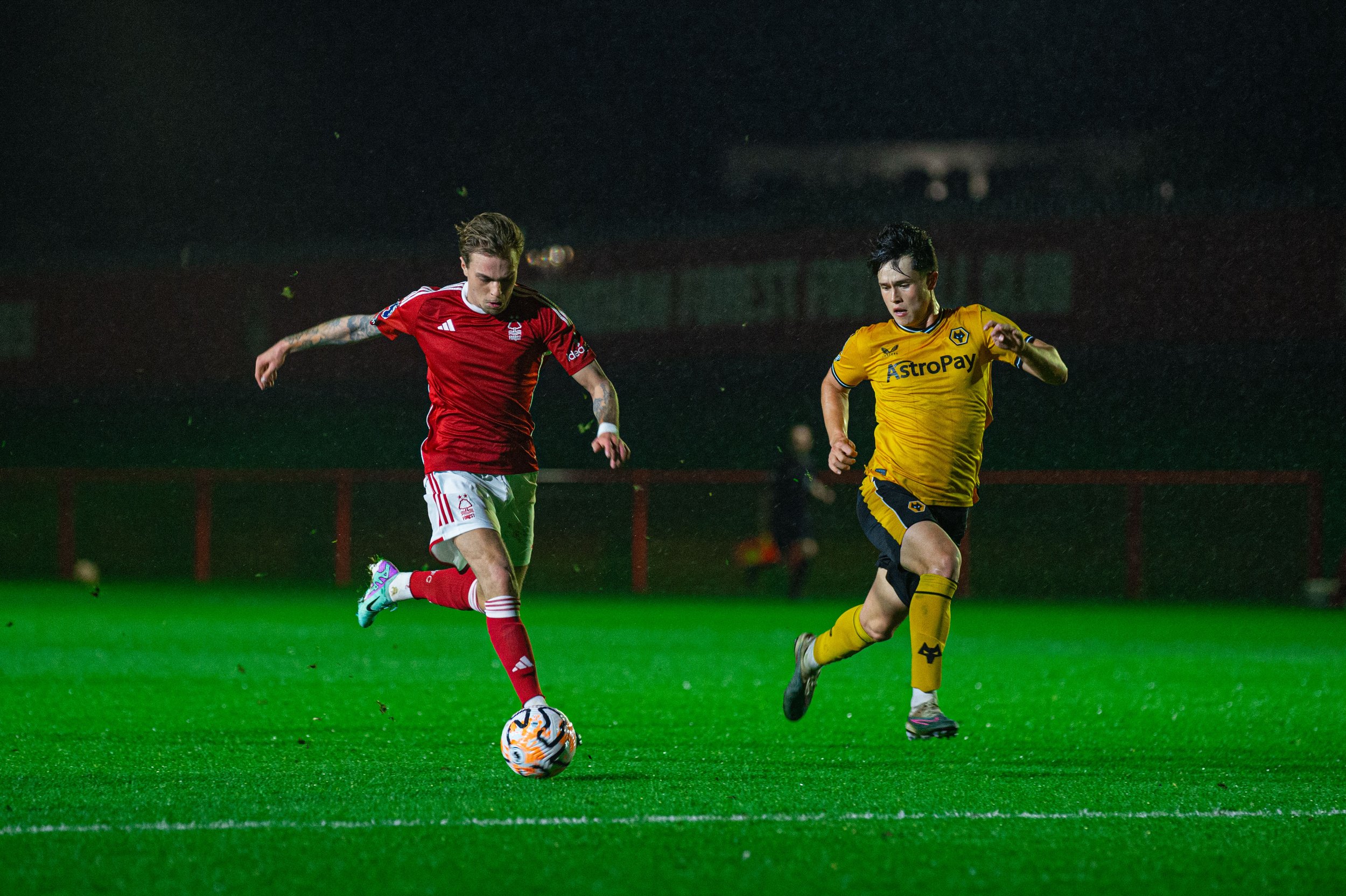 Two soccer players competing for the ball on a wet field at night