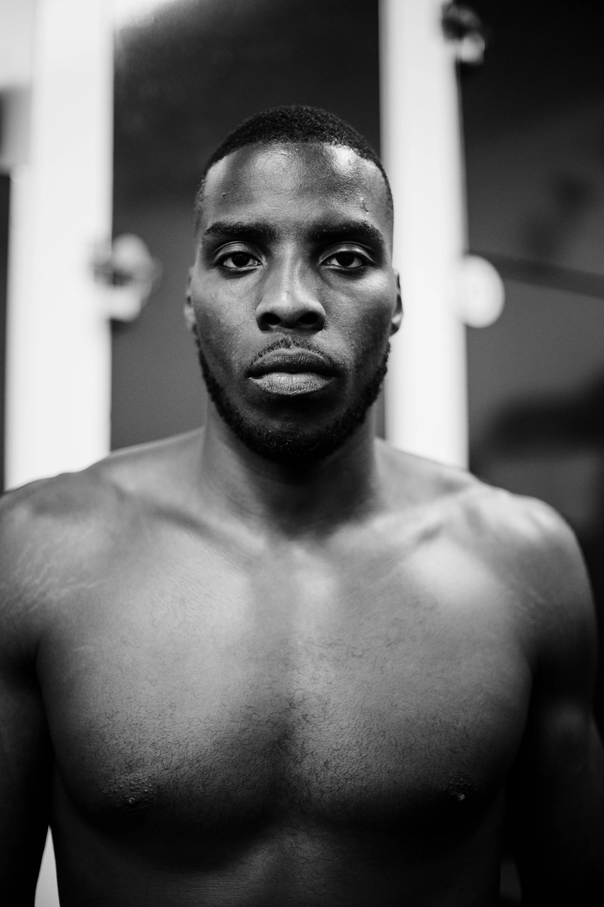 Black and white photograph of a shirtless man with a serious expression, standing in front of a mirror or reflective surface.