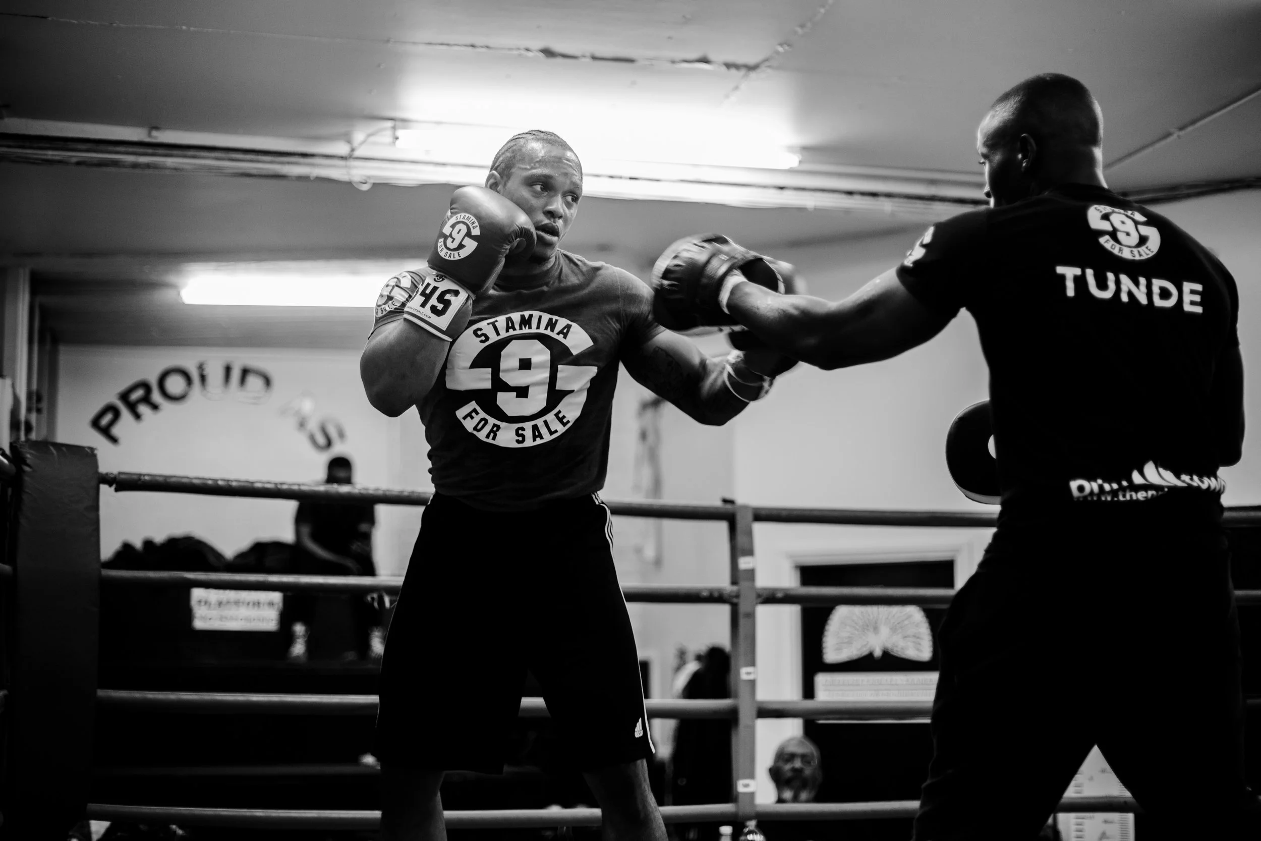 A person with dreadlocks in a boxing gym, sparring with a coach who is holding focus mitts.
