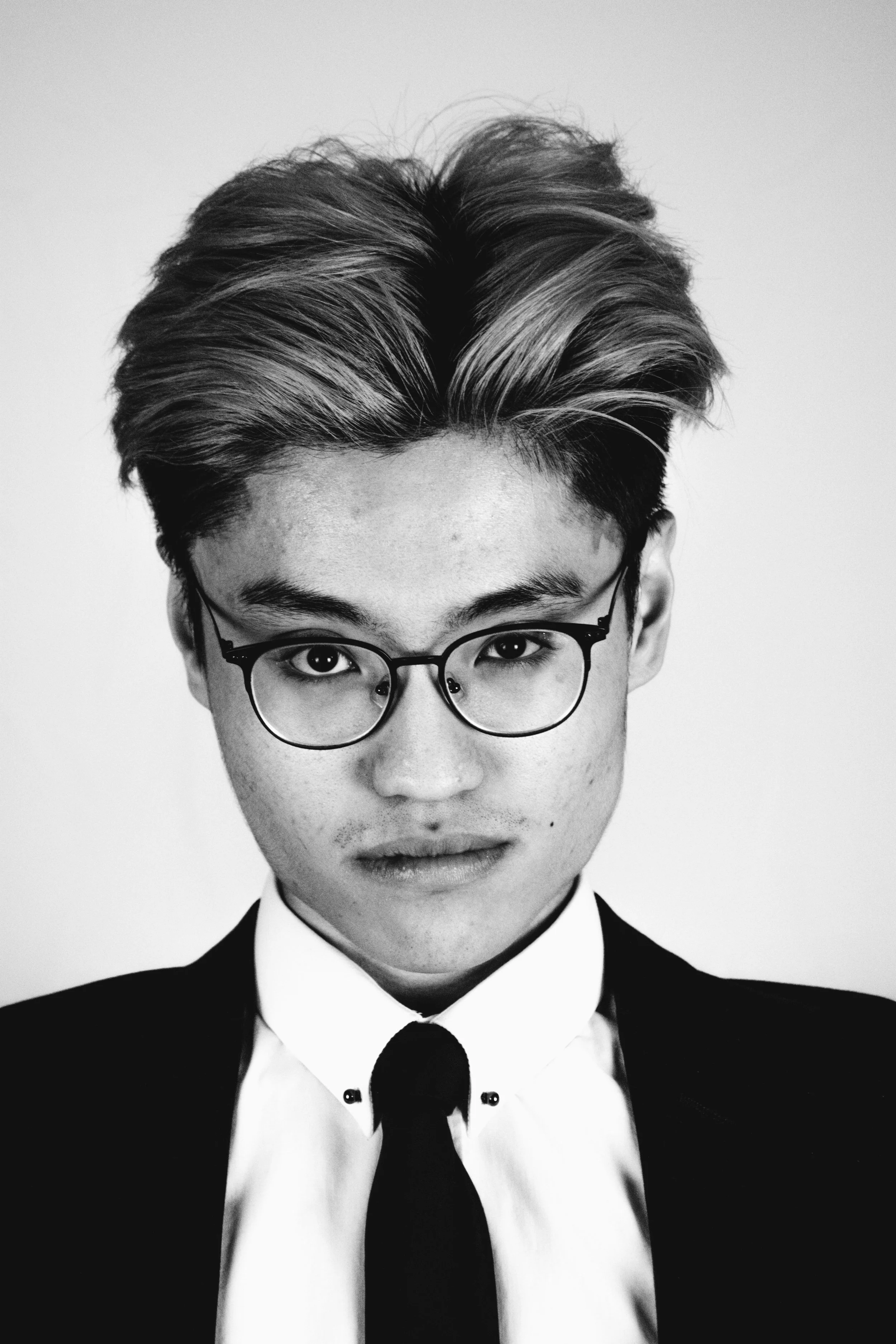 A black and white photo of a young man wearing glasses, a tuxedo, a bow tie, and a white shirt, with a confident expression.