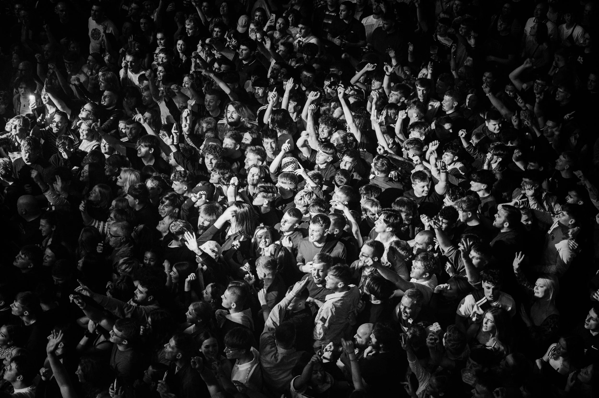 A large black and white crowd at a concert or event, with many people raising their hands and smiling.