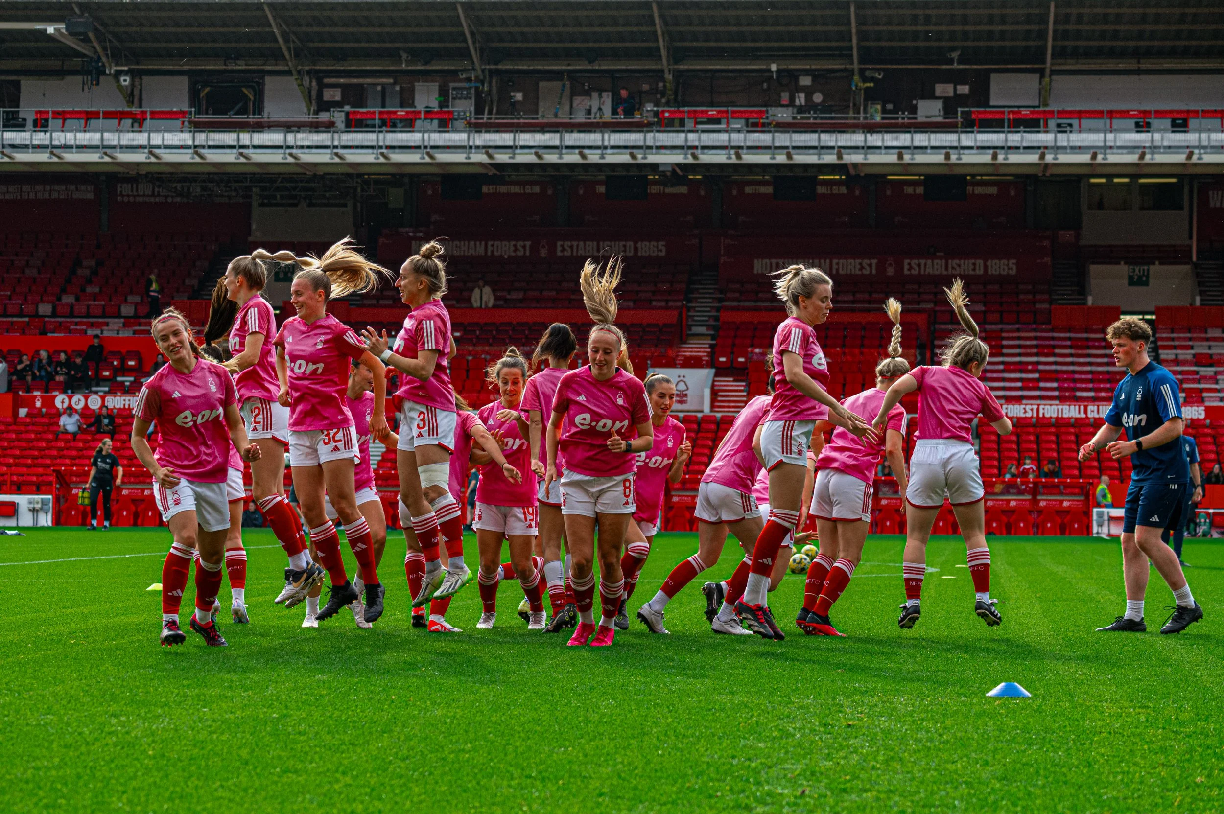 Women soccer players in pink jerseys warming up on the field during a game at a stadium.