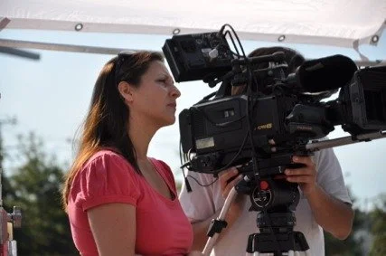 Erin McCahill on location behind a large video camera, filming a commercial on location