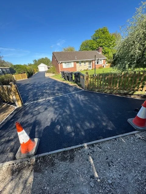 Freshly paved driveway with construction cones and a suburban house in the background.