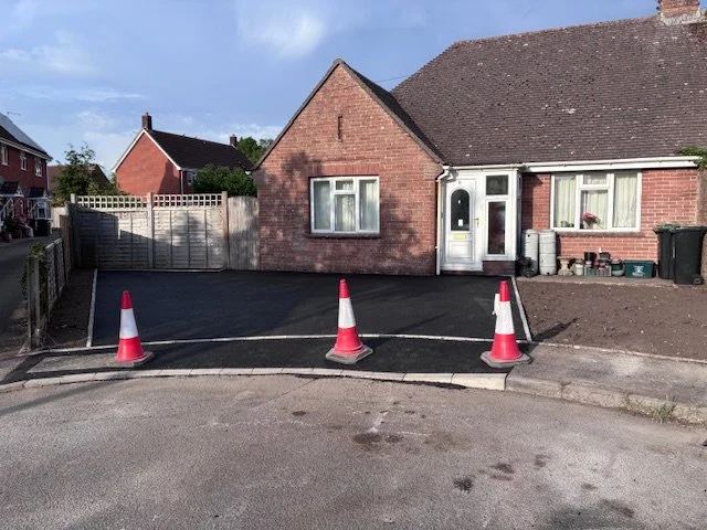 A recently paved driveway in front of a brick house with cones blocking parking.