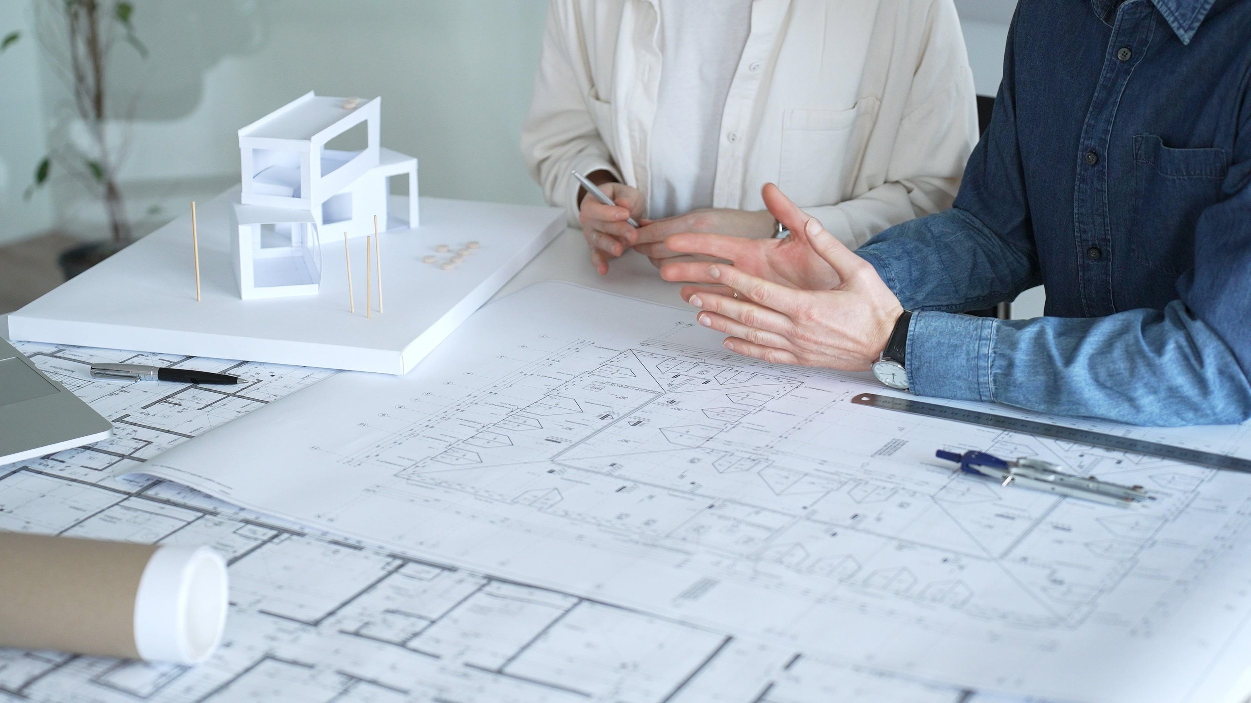 Two people discussing architectural plans and a small white model of a building on a table.