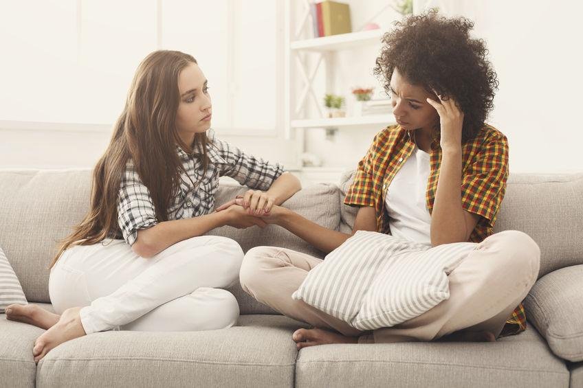 A young girl and an older woman sitting on a sofa, holding hands, with concerned expressions.