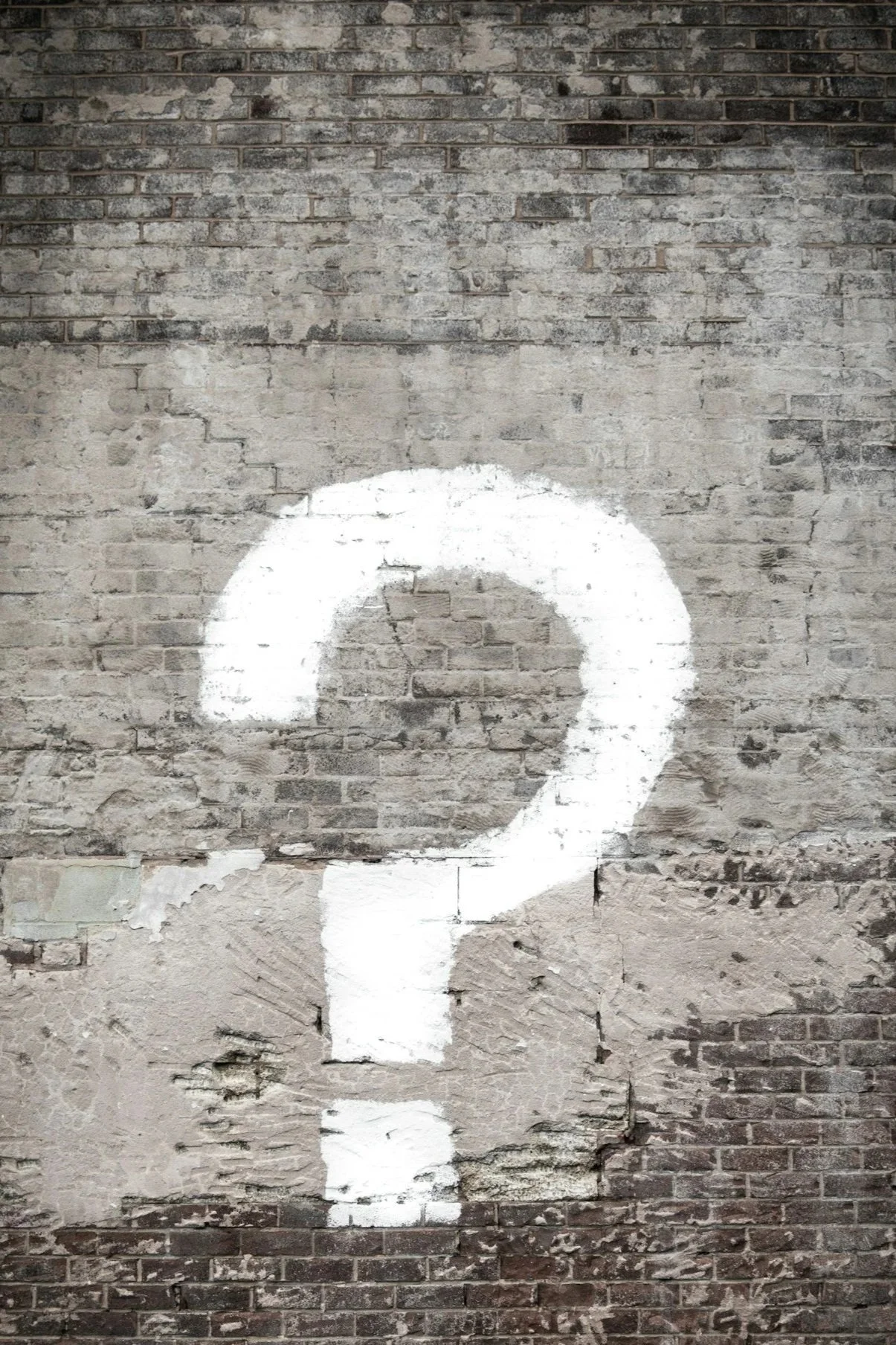 A white painted question mark on an old brick wall.
