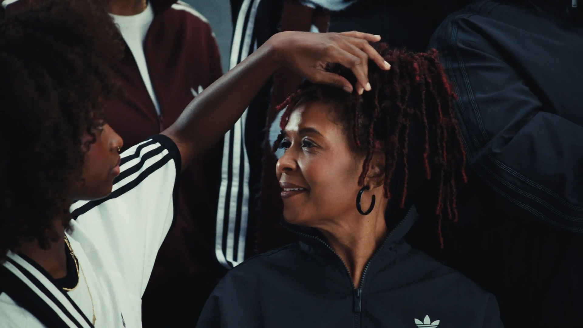 Een vrouw met dreadlocks krijgt een hoofdknuffel van een andere vrouw met een glimlach, beide vrouwen dragen sportkleding.