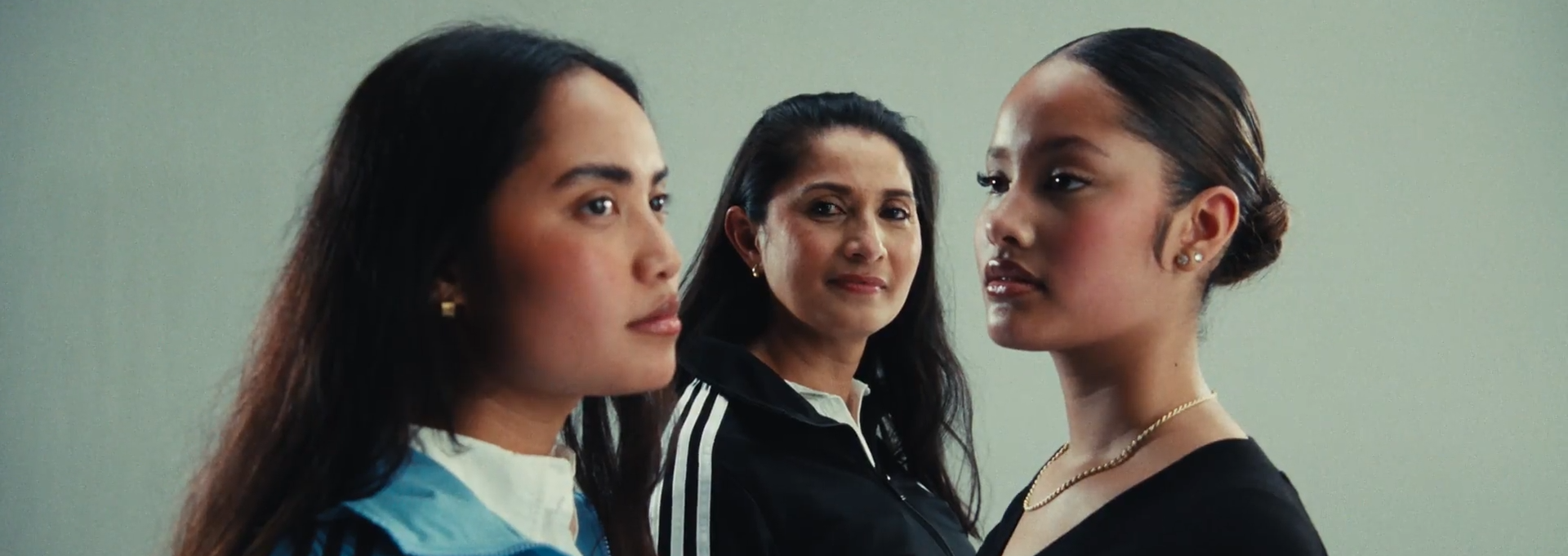 Drie vrouwen staan dicht bij elkaar in profiel, kijkend naar rechts. Ze lijken in een discussie of gesprek, met een neutrale achtergrond.
