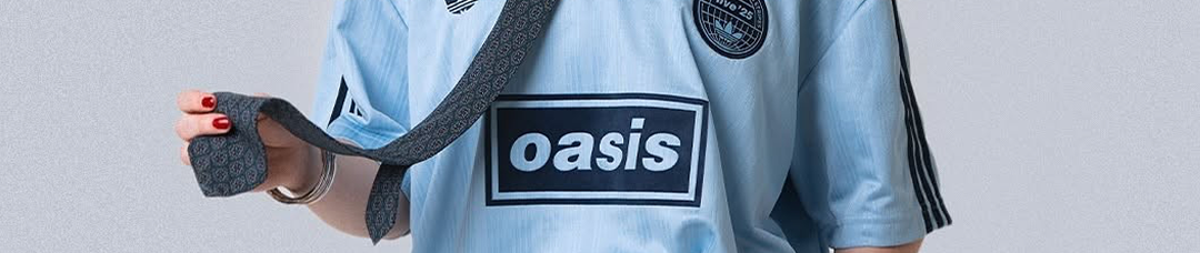 Close-up van een persoon in een lichtblauw sportshirt met logo en een tas over de schouder, tegen een grijze achtergrond.
