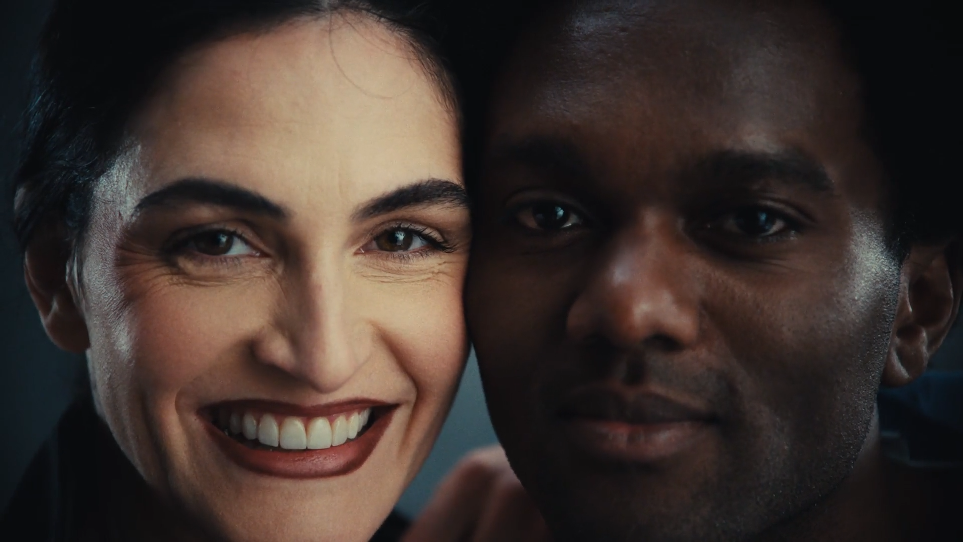 Close-up van een lachende vrouw met licht huid en donker haar naast een man met donkere huid en korte haar, beiden dichtbij elkaar.