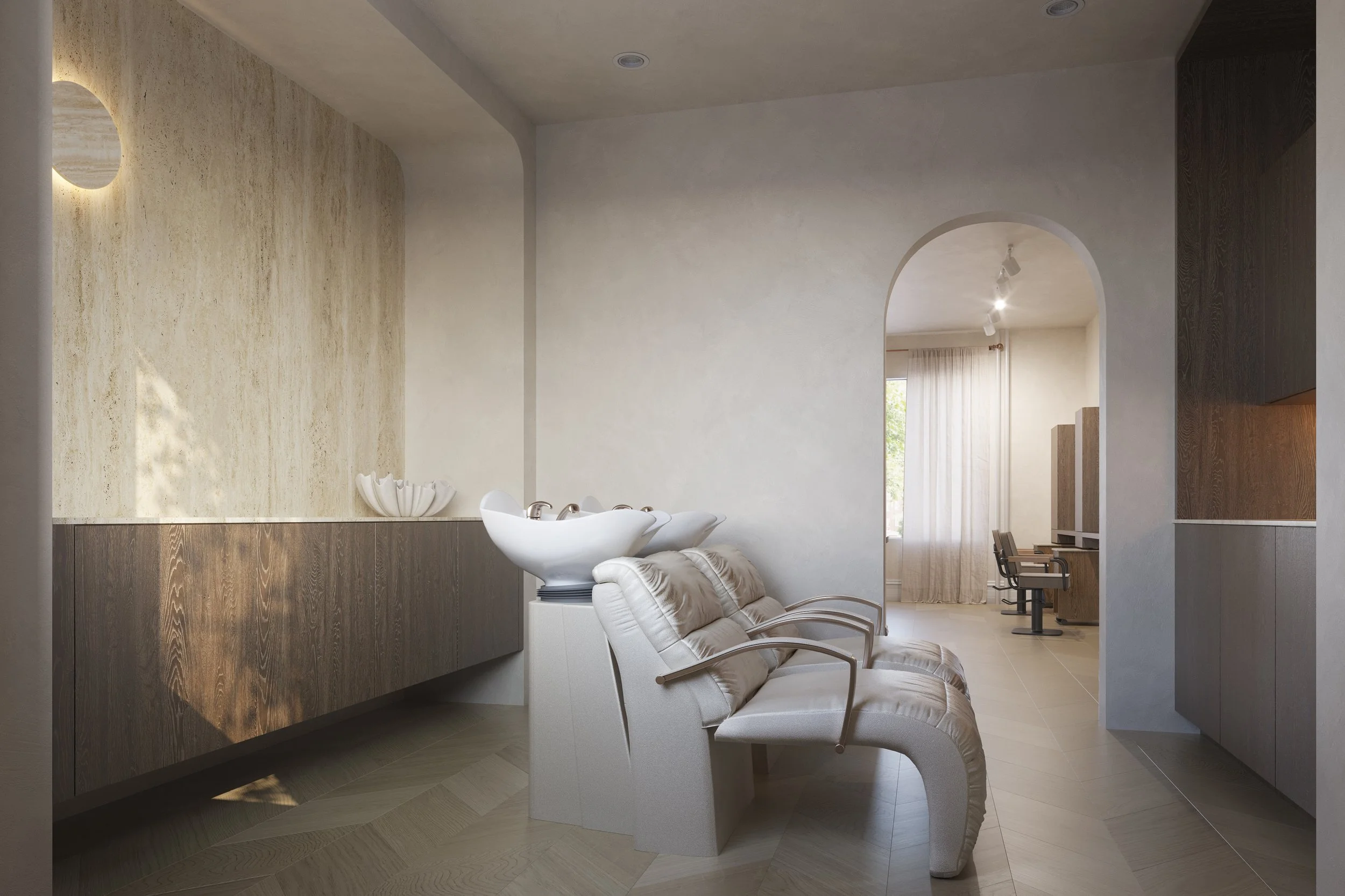 Two hairdresser chairs and sinks sit next to eachother within a beautiful beige salon space filled with natural light.