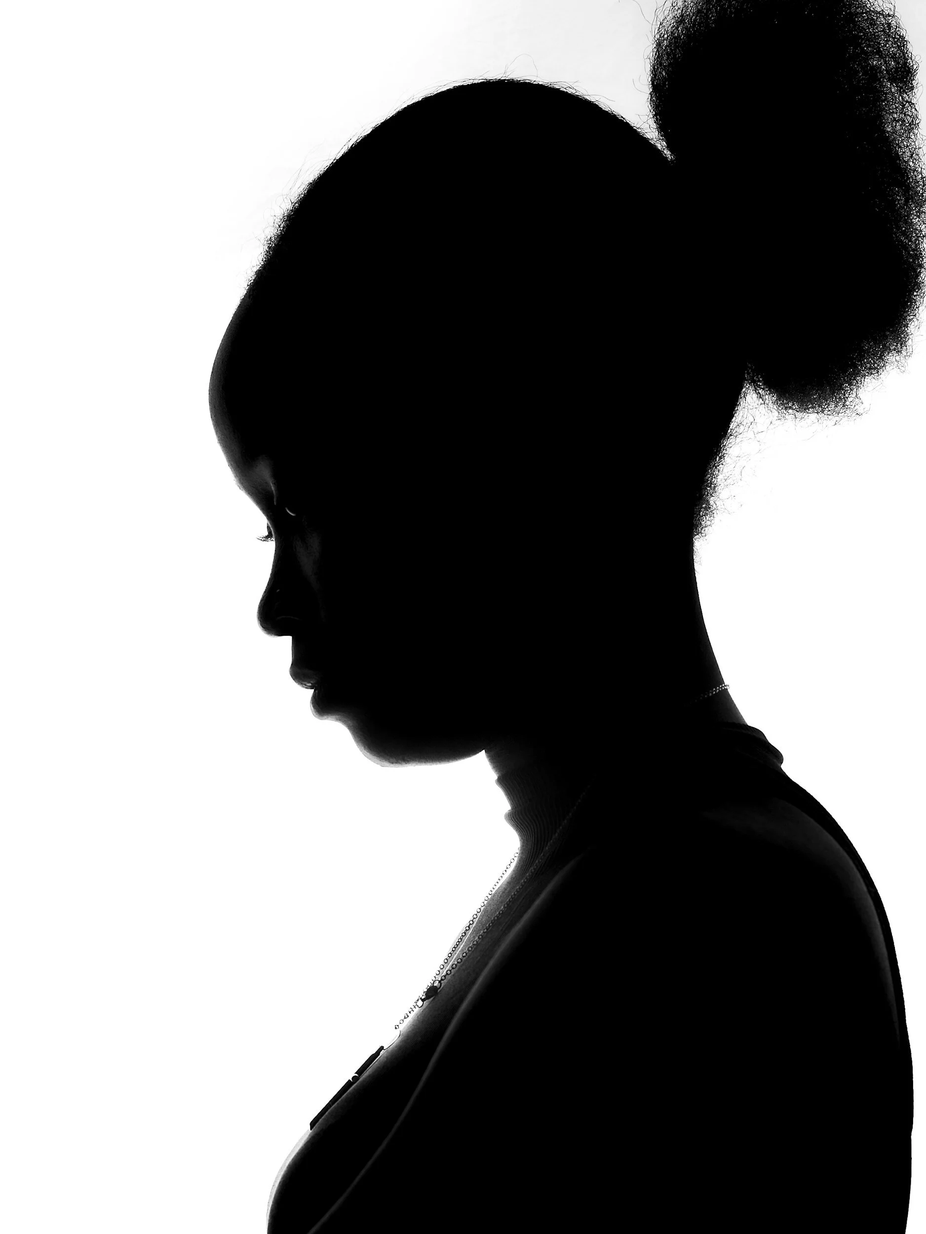 Silhouette of a woman with a natural hairstyle, looking downward, with a high contrast black and white effect.