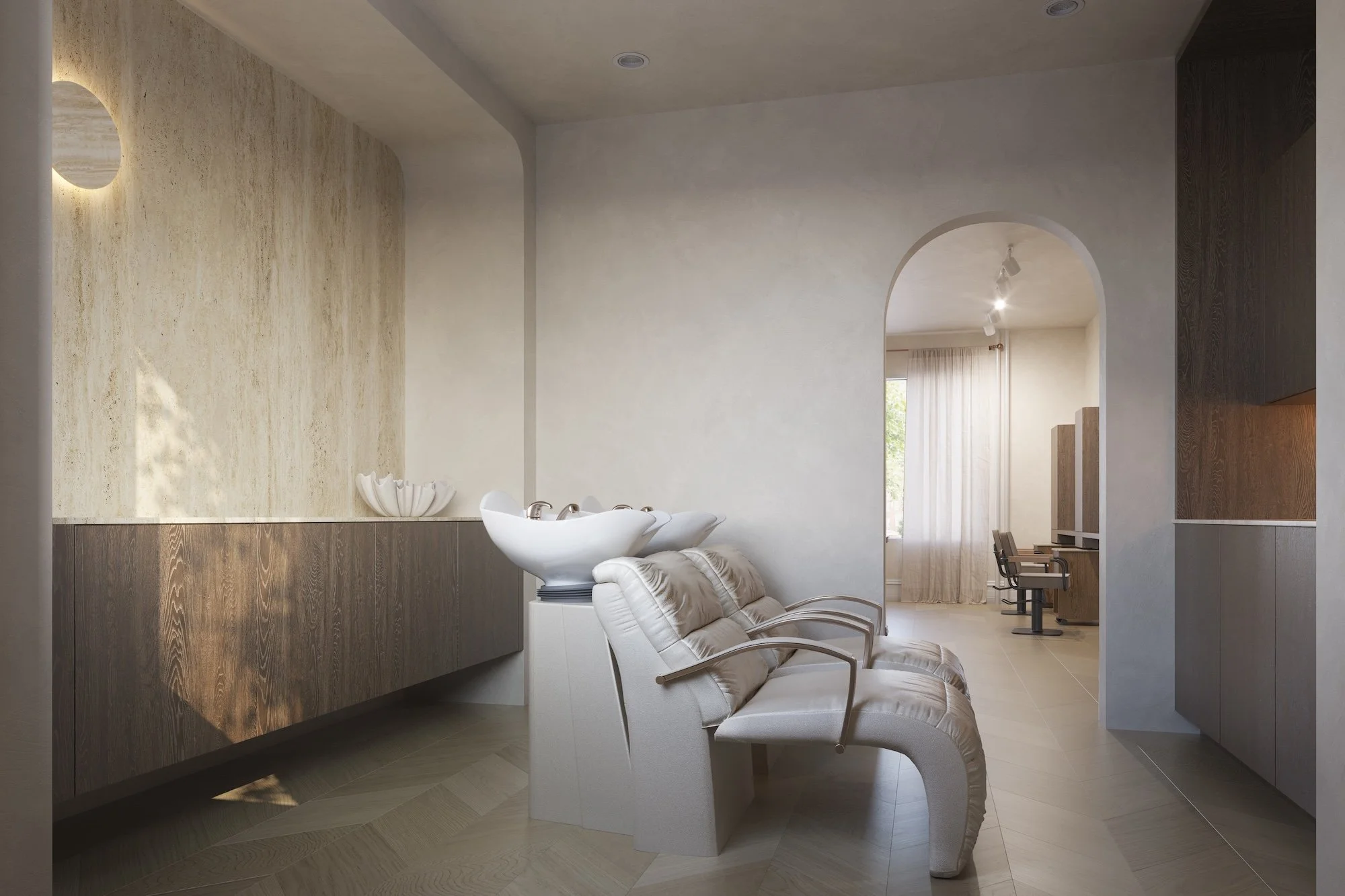 Modern salon interior with beige and brown color scheme, comfortable chairs, a white sink, natural light from large window with sheer curtains, and arched doorways.
