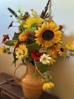 A flower arrangement with sunflowers and more in a ceramic vase on a wooden table