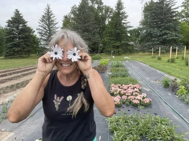 Shari Froelich, owner of Harmony Acres, holding two white flowers over her eyes while standing in her farm