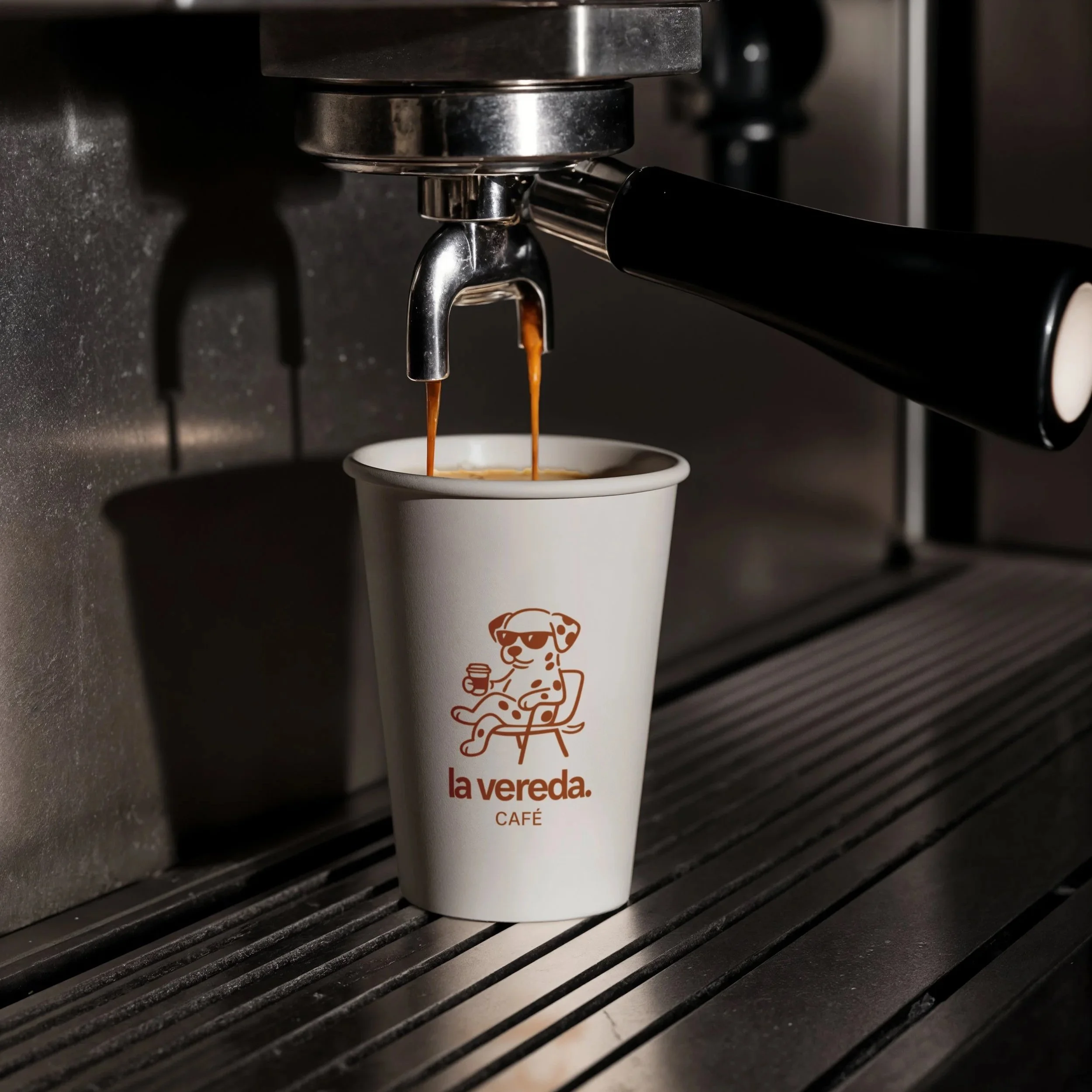 Café espresso siendo preparado en una máquina de café, con dos gotas de café cayendo en una taza blanca con el logo de La Vereda.