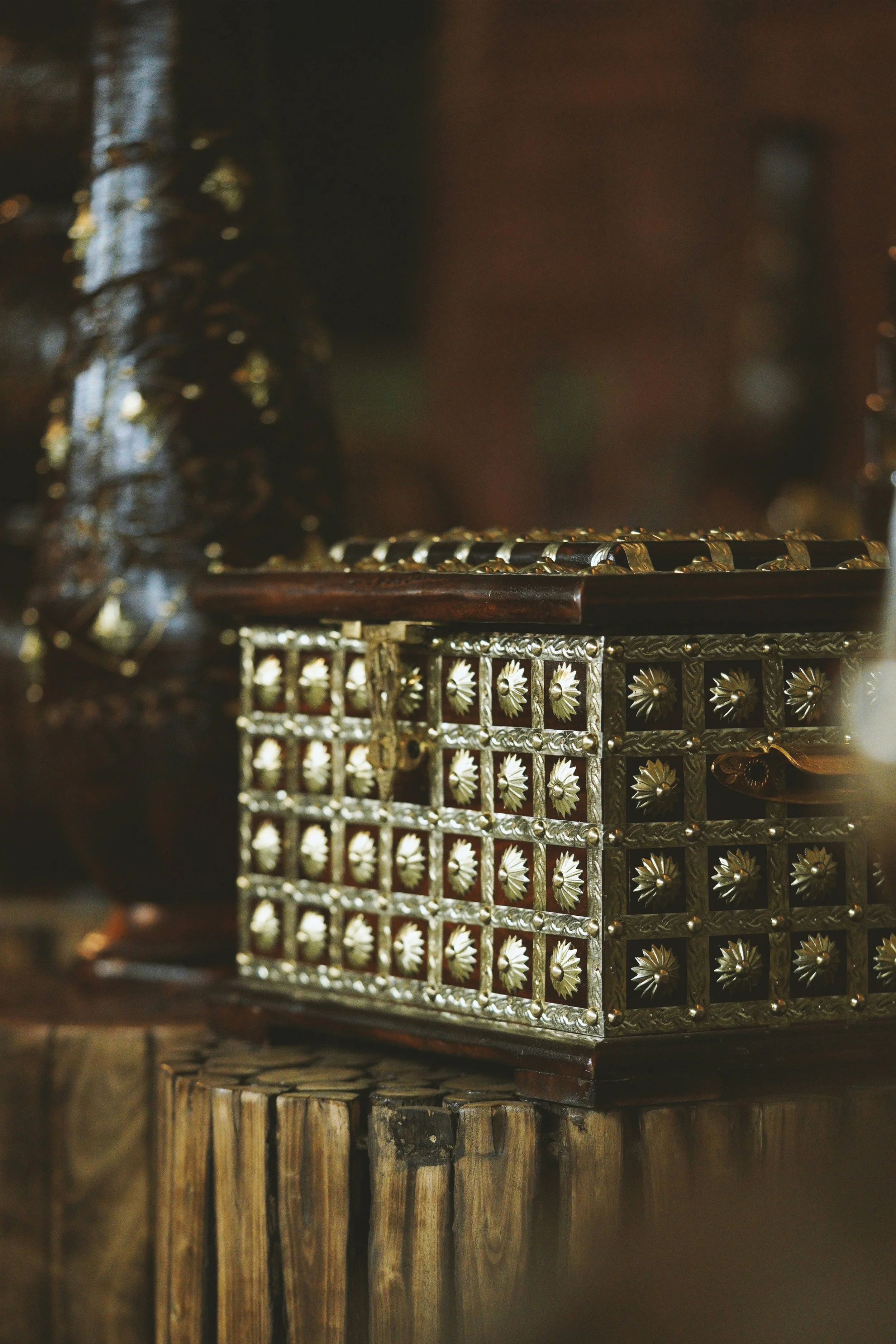 Close-up of ornate, decorative metalwork with gold and silver accents, featuring intricate floral patterns, placed on a dark wooden surface.