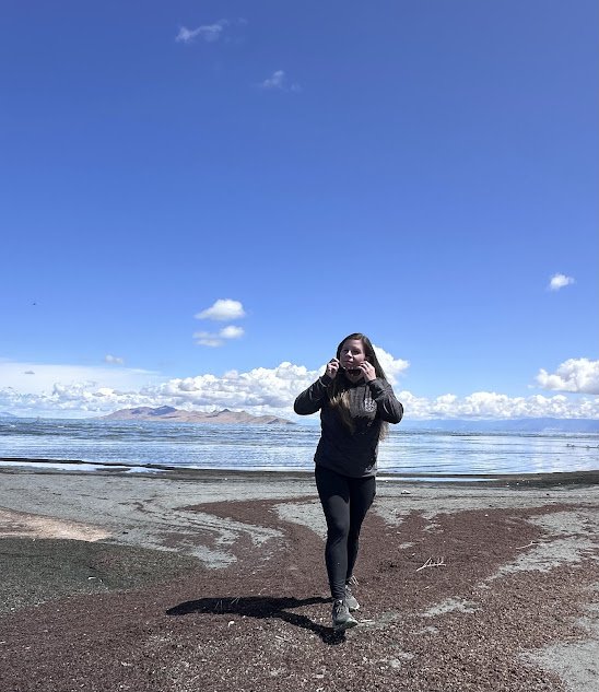 Person walking on a beach under a blue sky, holding headphones.