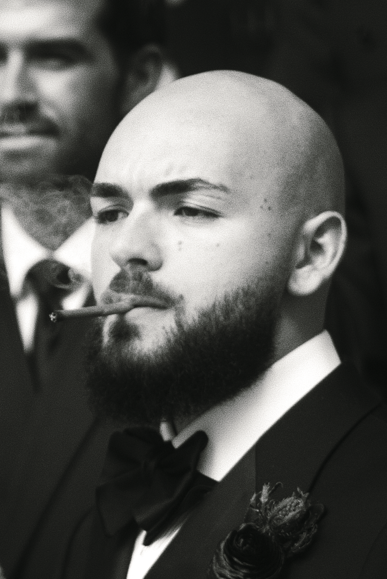 Black and white photo of a man with a beard, wearing a tuxedo with a bow tie, smoking a cigar.