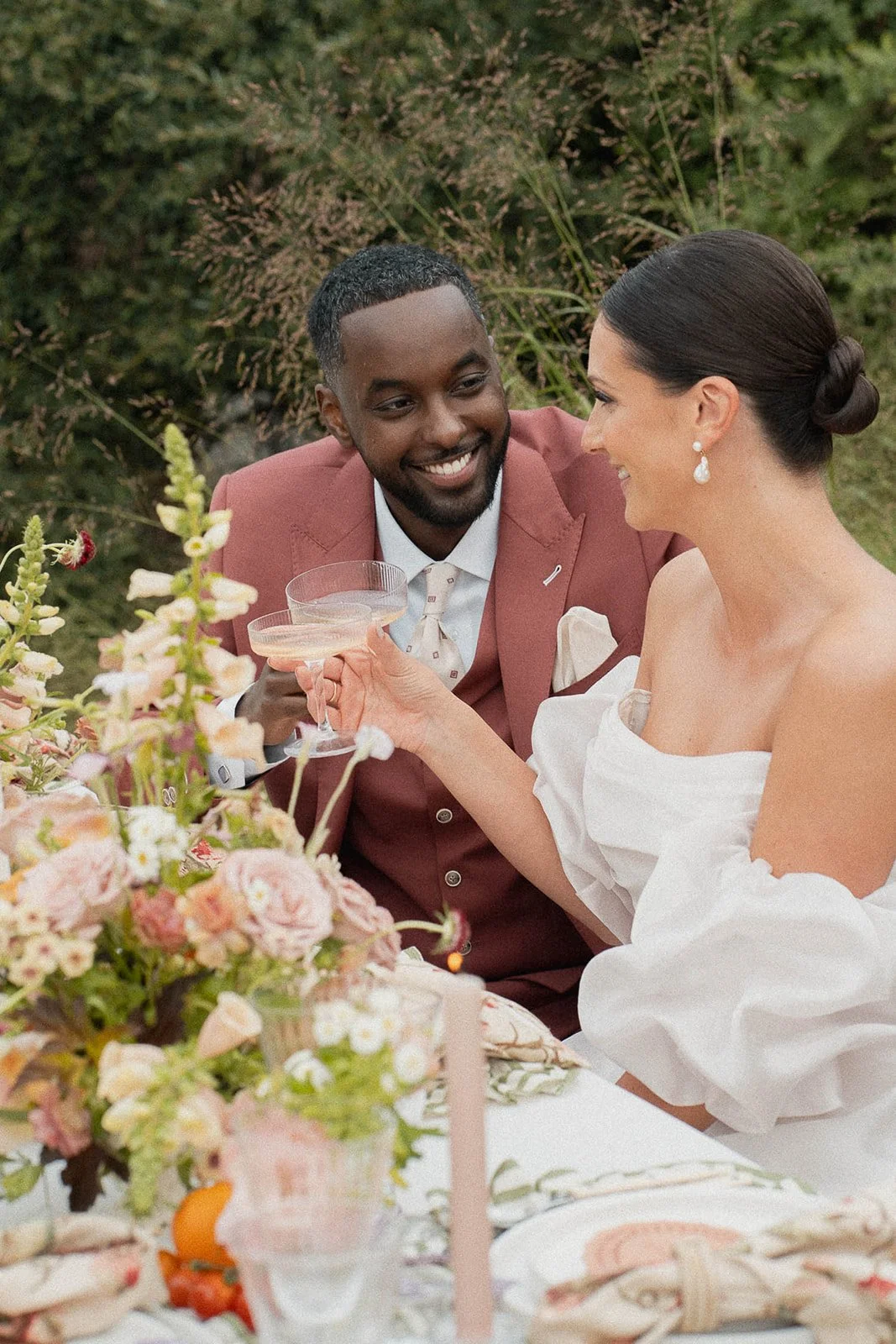 Bride and groom sharing a toast at an outdoor picnic table decorated with flowers.