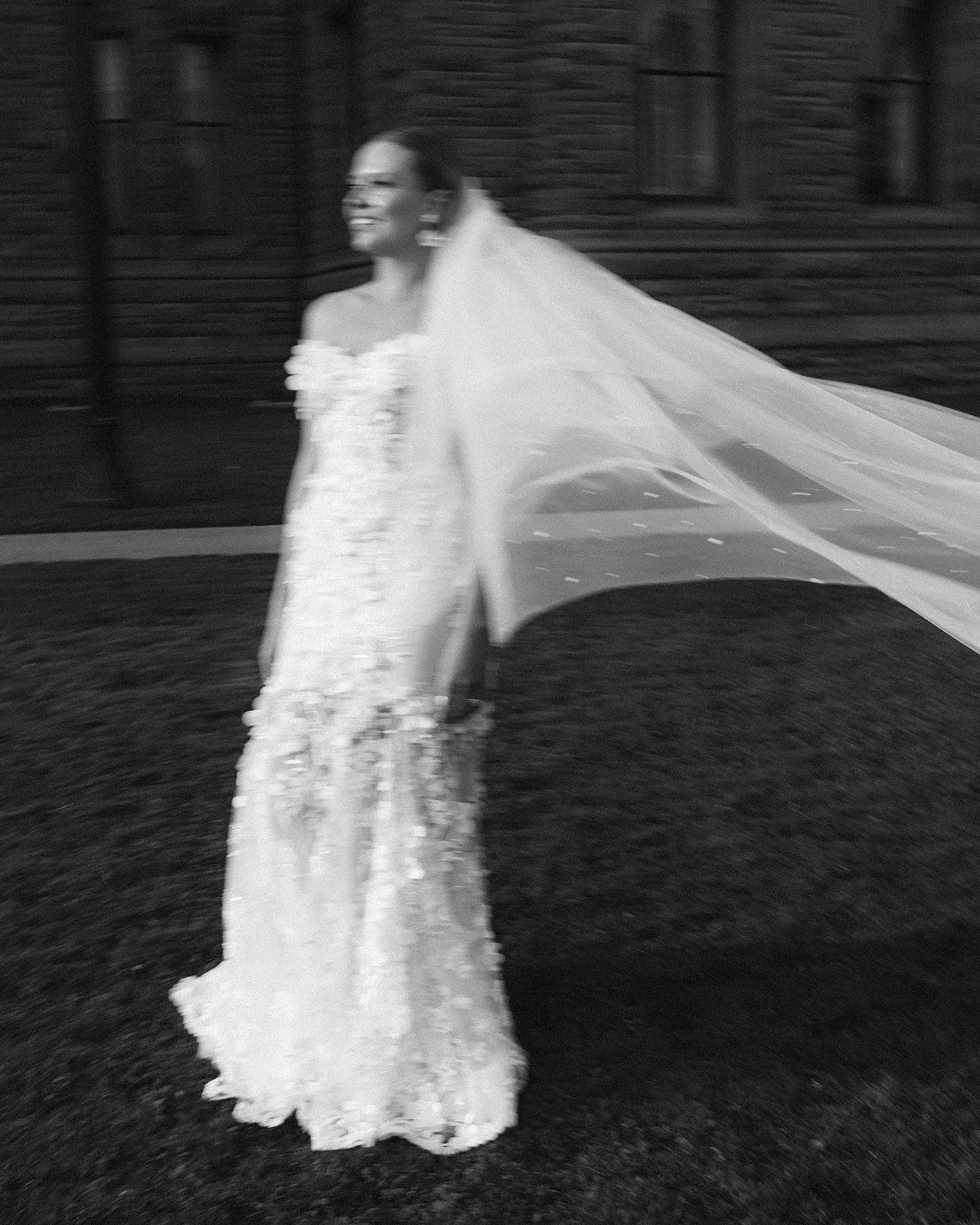 A woman in a wedding dress with a long train and a veil, smiling as she walks outside in downtown Toronto.