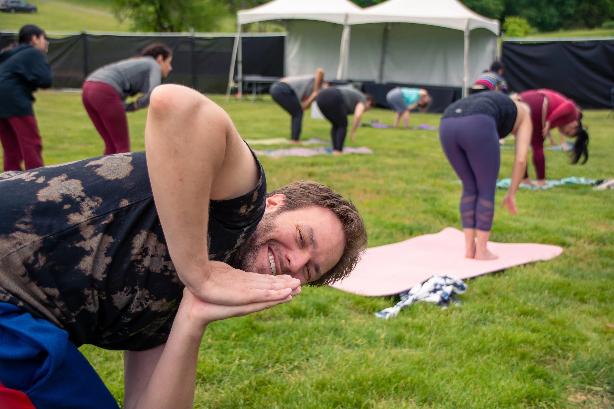 Group of people practicing yoga outdoors on grass, with tents in the background, during daytime.
