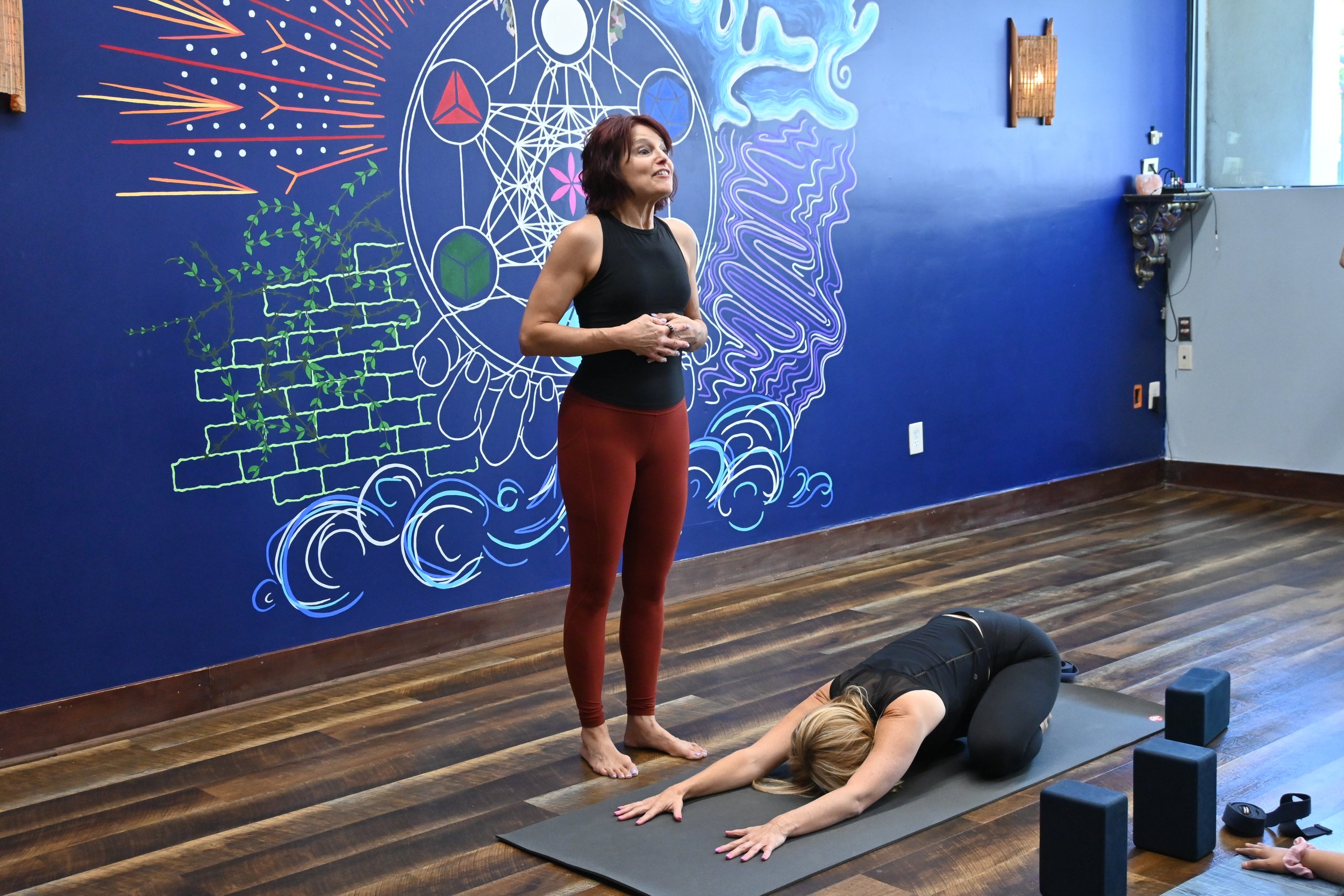 Women practicing yoga in a studio with a colorful abstract wall mural.