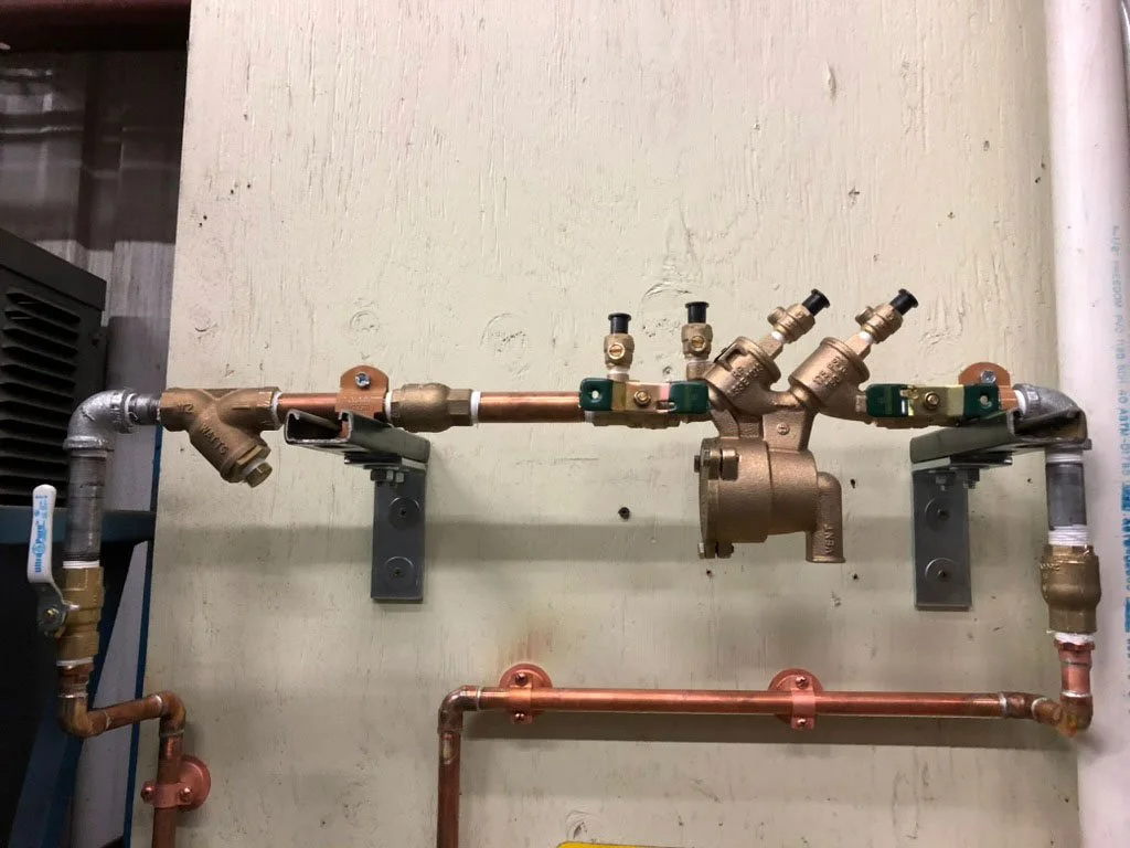A plumbing manifold with copper and brass pipes, valves, and fittings mounted on a wall.