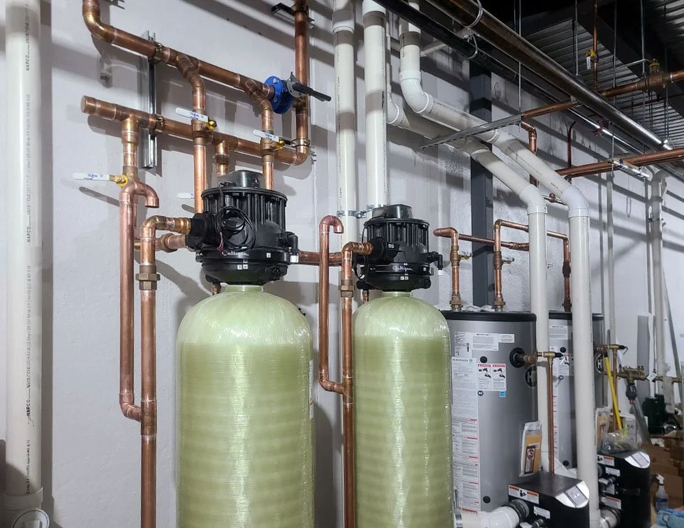 Indoor plumbing and water filtration system including copper pipes, large green tanks, and water heaters.