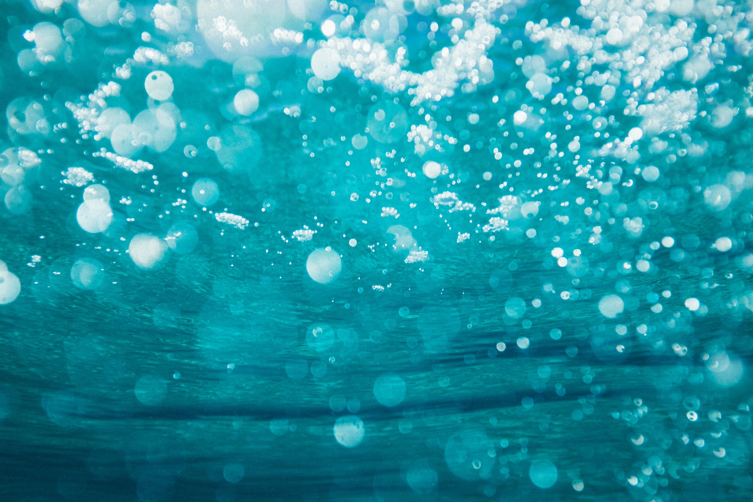 A close-up view of water droplets on a surface with a blue-green background, creating a bokeh effect.
