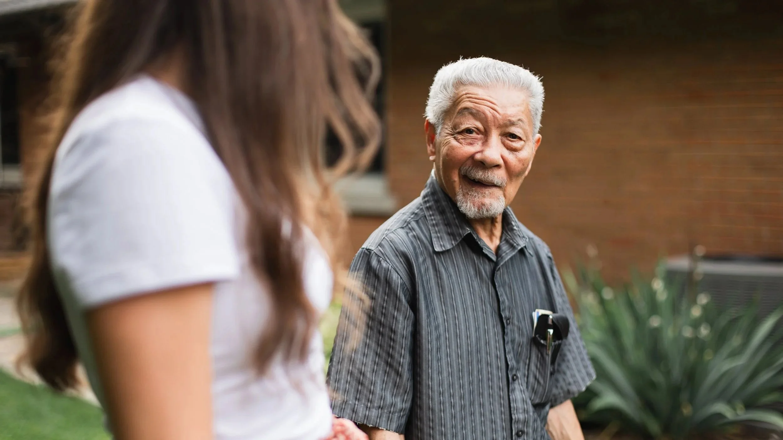 Better Days companion care for seniors in Kitchener-Waterloo. An elderly man with white hair and a beard smiling and talking to a woman with long reddish-brown hair, outside near a brick building.