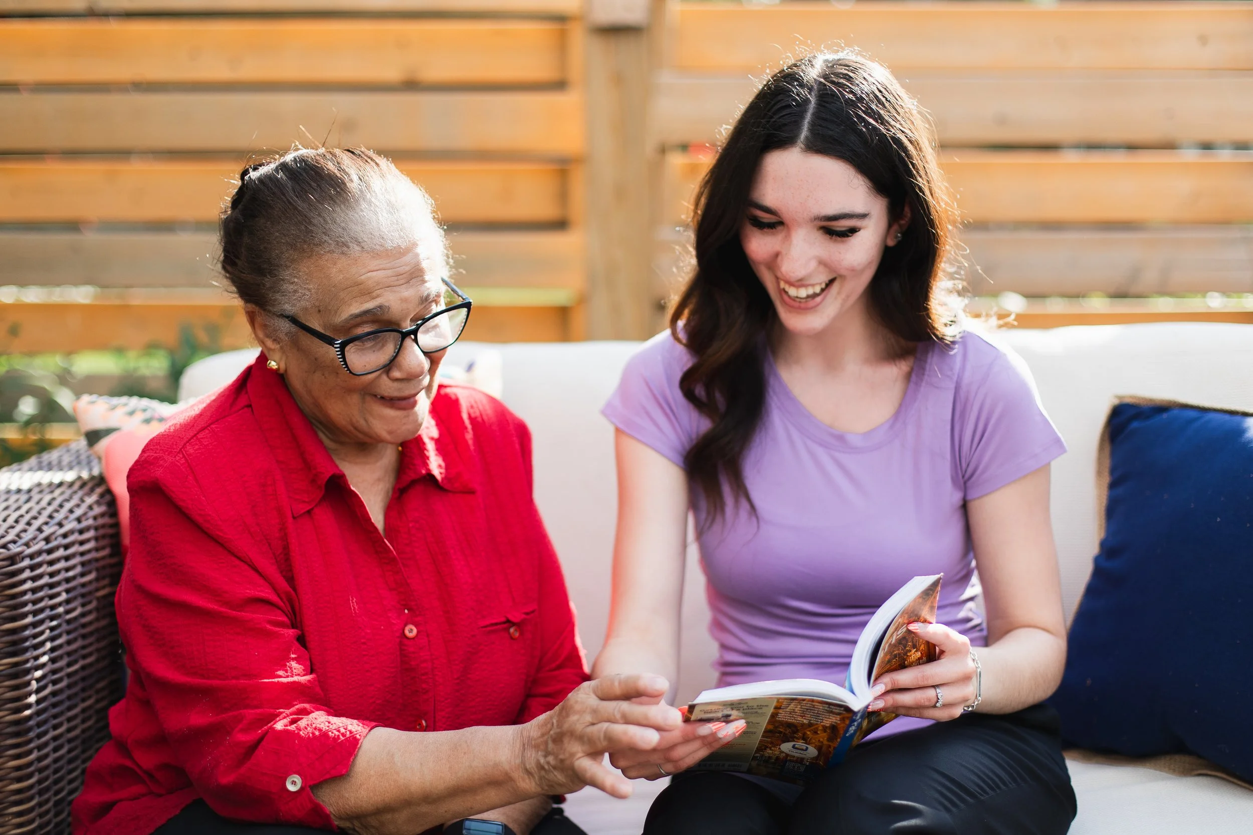 Better Days companion care for seniors in Kitchener Waterloo. An elderly woman and a young woman sitting outside on a couch, both looking at a magazine and smiling.