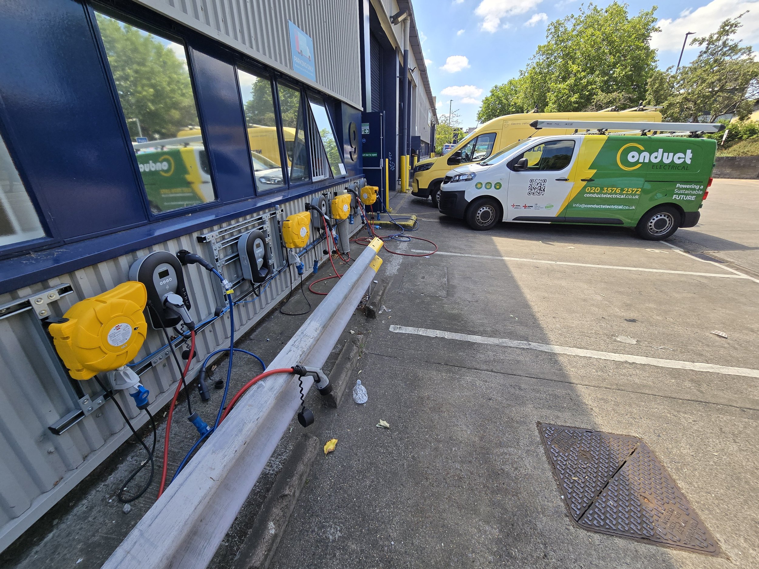 Electrical service vehicles parked outside a building, with electrical equipment and wires connected to the building's exterior.