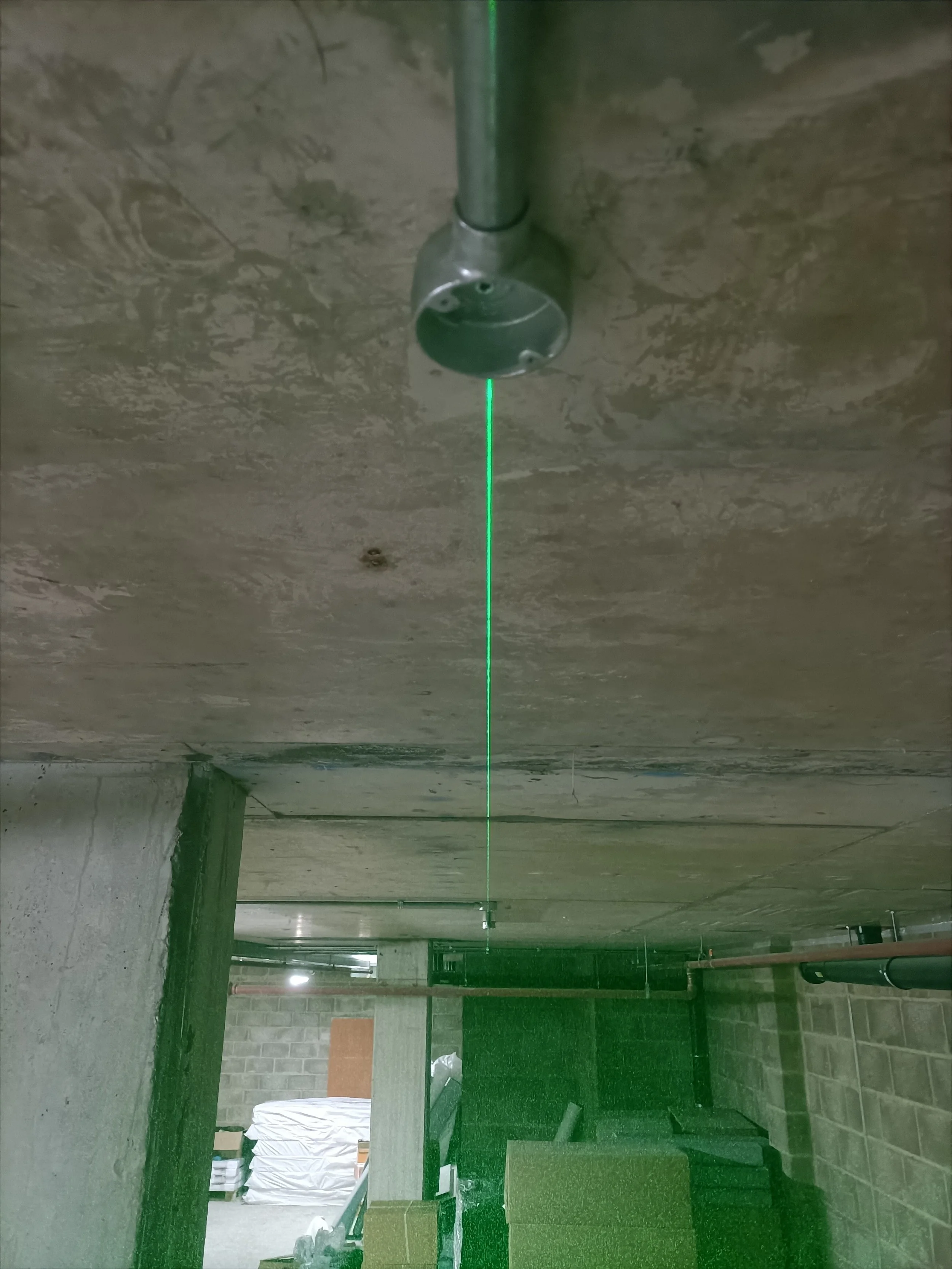 Construction site with exposed brick and concrete walls, pipes, some furniture, and a green laser line running from the ceiling to the floor.