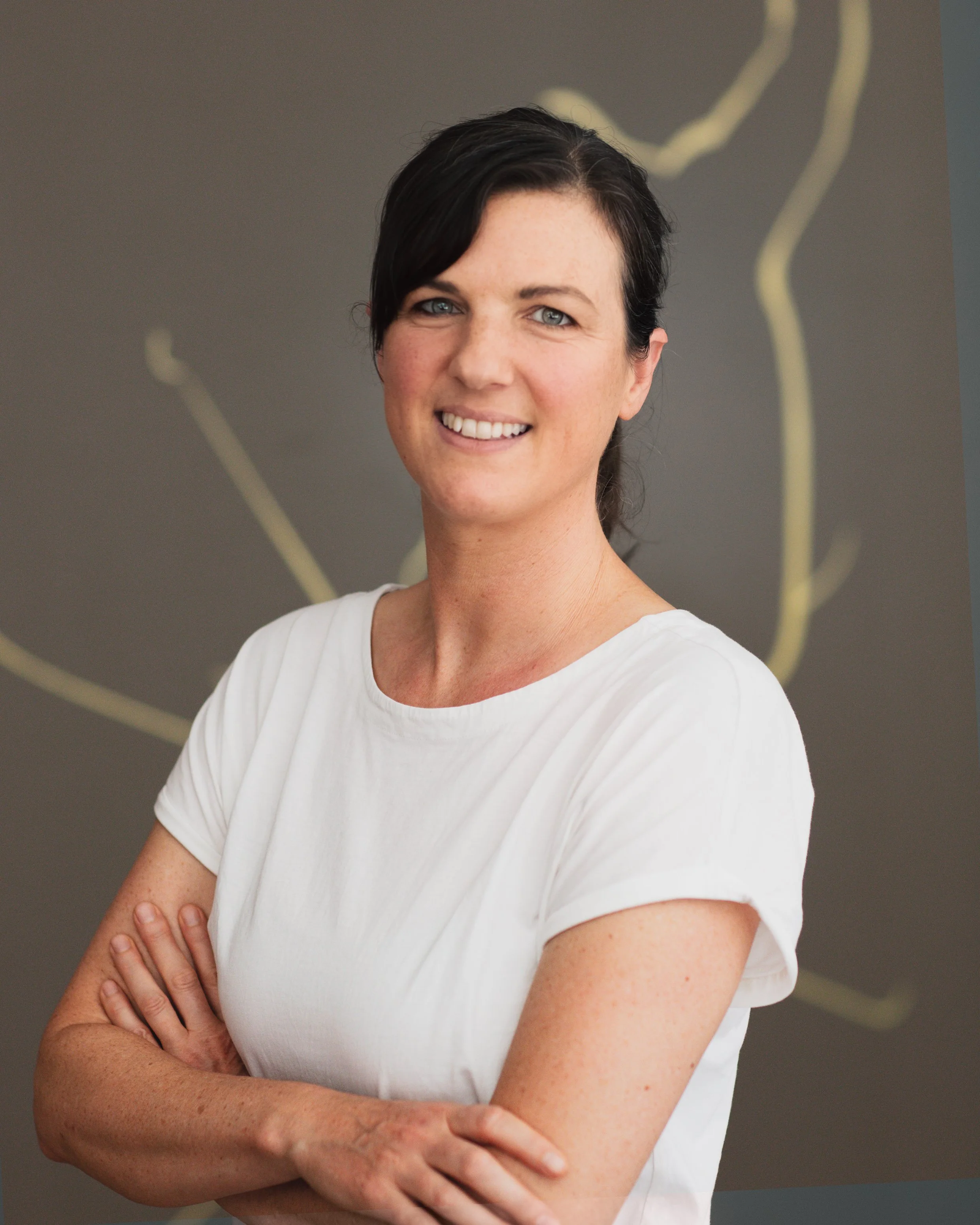 Portrait de Anaïs Gauthier, physiothérapeute chez PhysioAir, cheveux courts et sombres, portant une chemise blanche à manches courtes, sourit en regardant vers l'objectif, avec un fond gris décoré de lignes jaunes.
