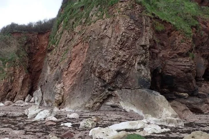 Steep rocky cliffside with patches of green vegetation and rocks at the base.