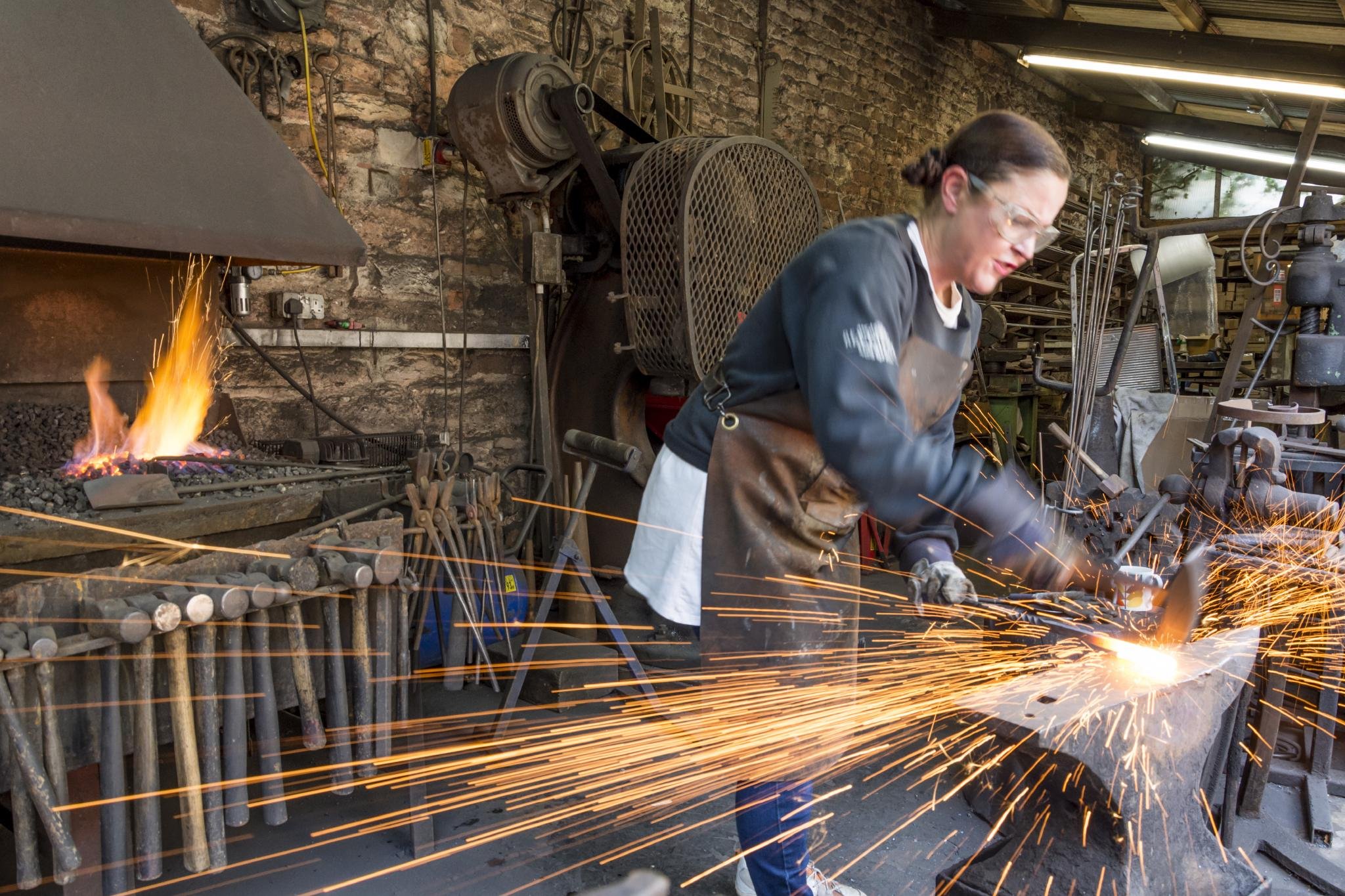 A woman working as a blacksmith in a workshop, using tools to shape metal with sparks flying around.