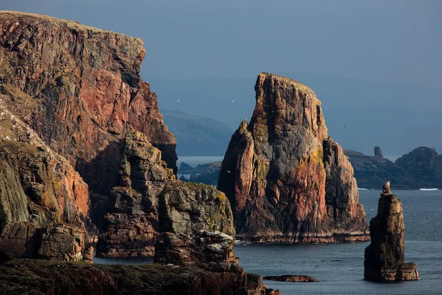 Cliffs and sea stacks along a rugged coastline with ocean in the background.