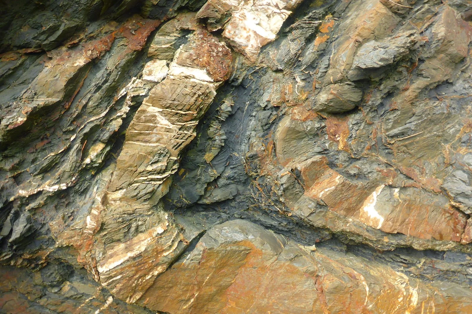 Close-up of layered, multi-colored rock formations with primarily dark gray, brown, and rust hues.