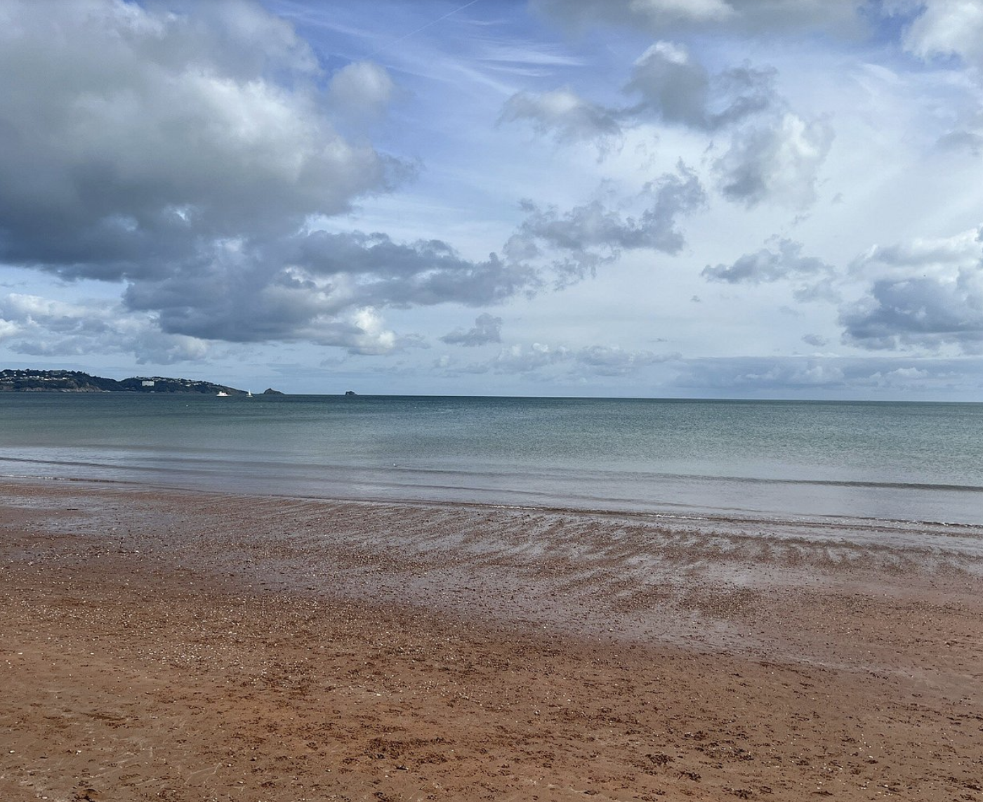 A sandy beach with gentle waves and a calm ocean under a partly cloudy sky.