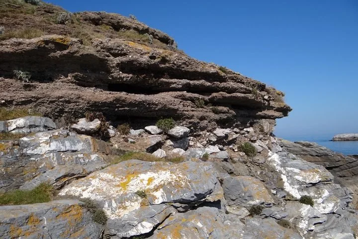 Rocky coastal landscape with layered cliffs and ocean in the background under a clear blue sky.