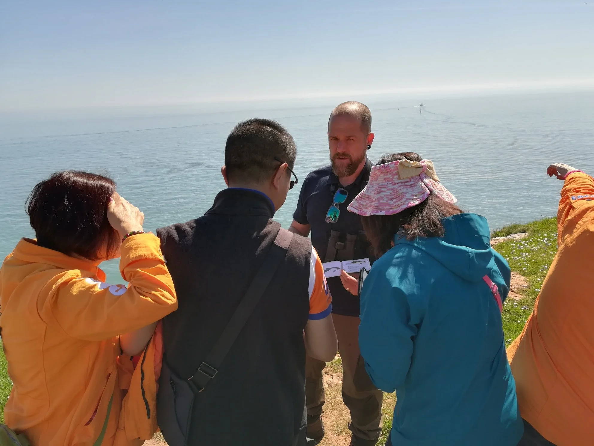 Group of people standing outdoors near a body of water, engaged in conversation on a cloudy day.