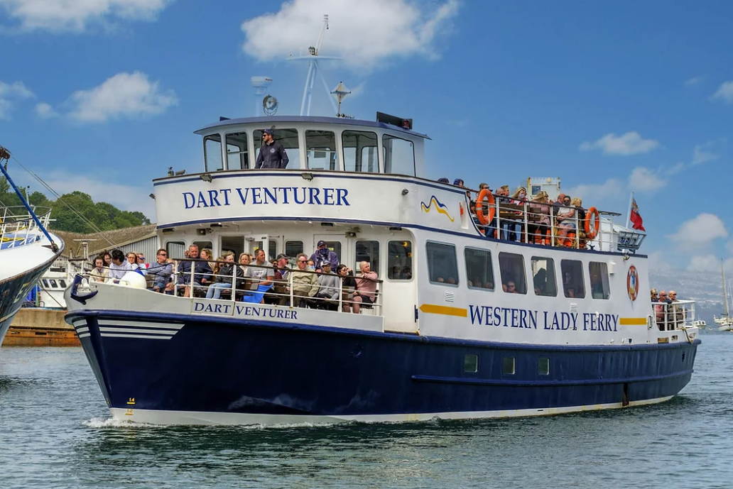 A boat named Dart Venturer with many passengers on board, sailing on a body of water under a partly cloudy sky.