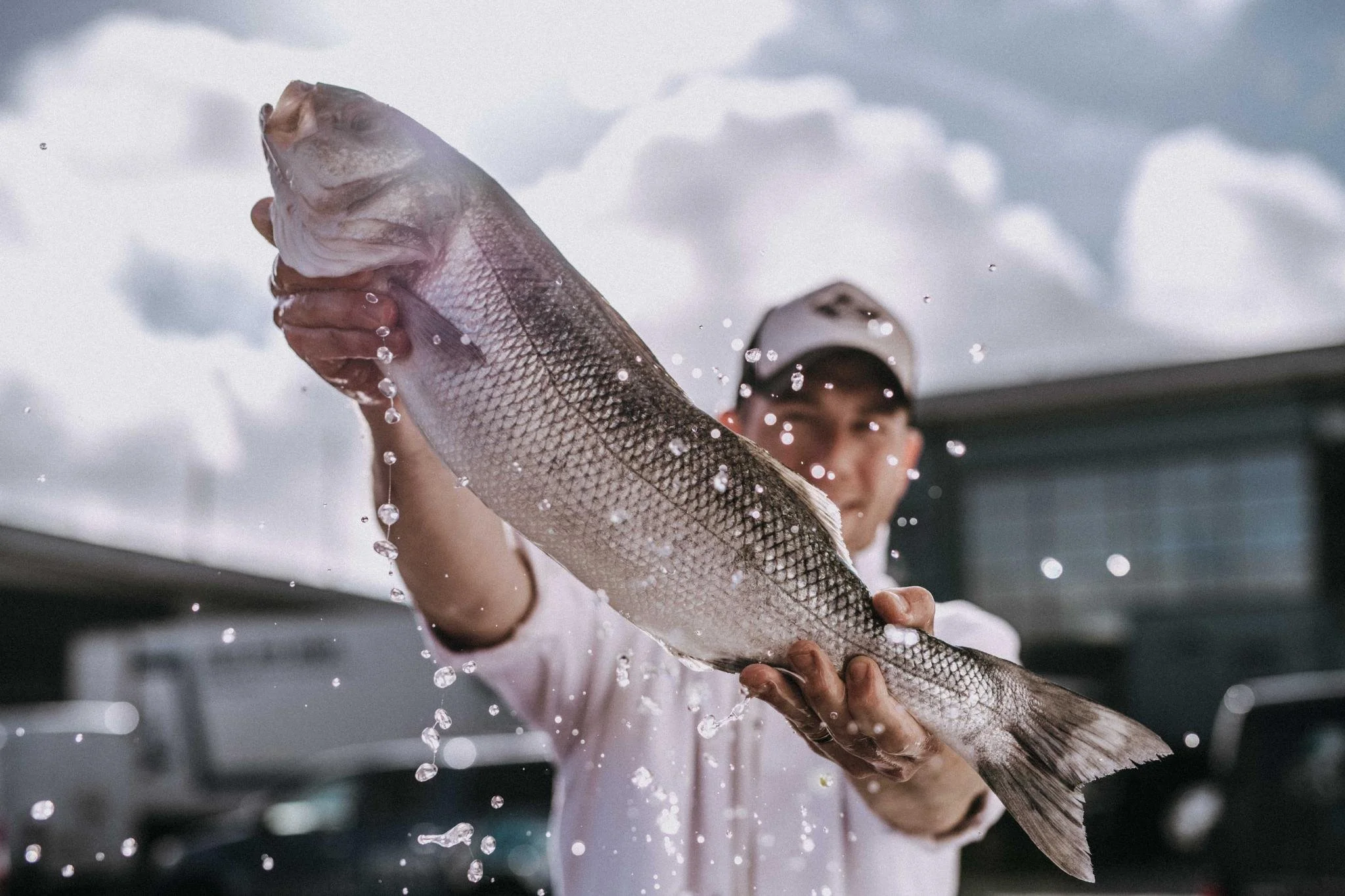 Person holding a large fish with water droplets falling, outdoors.