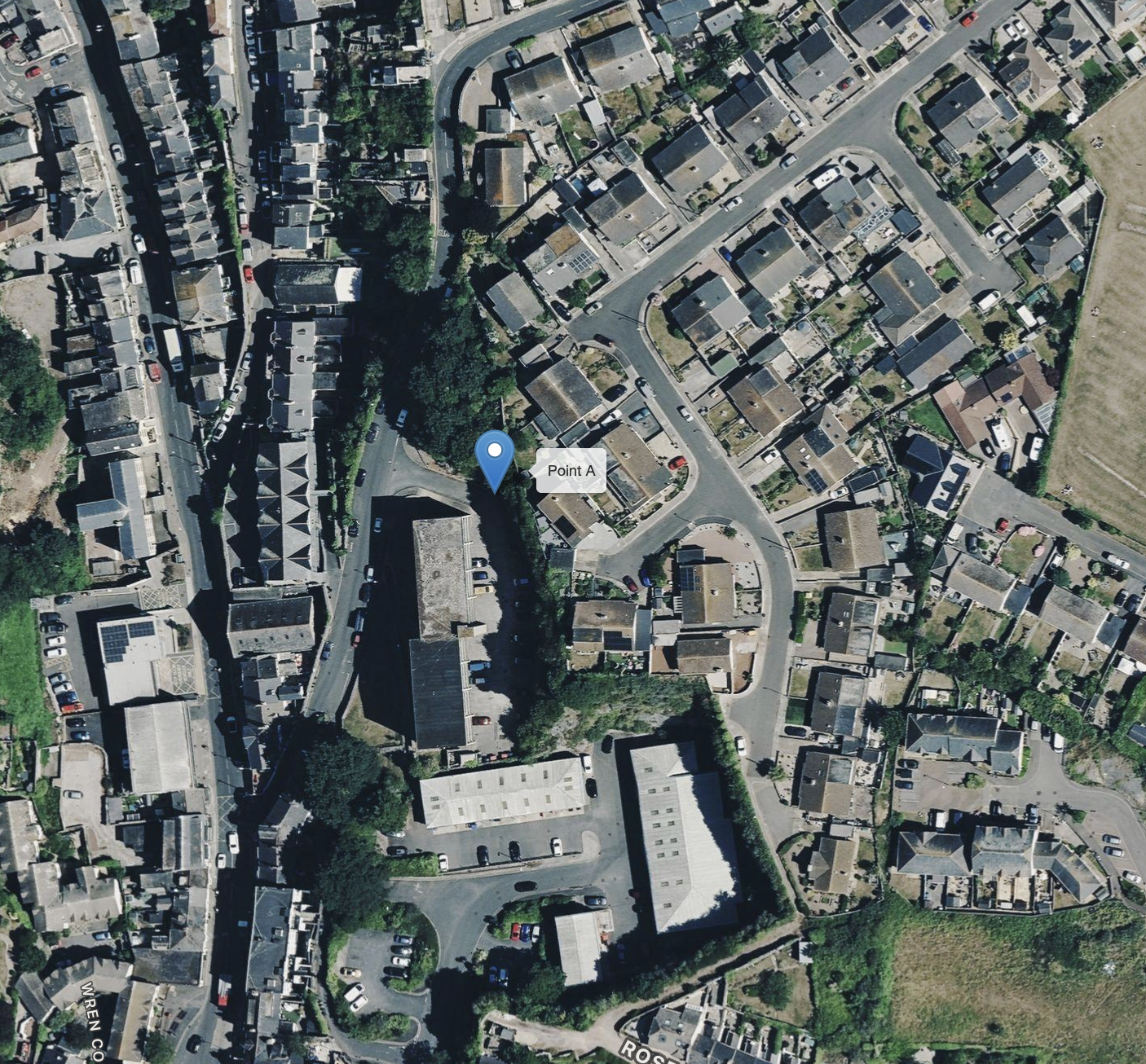 An aerial view of a residential neighborhood with winding streets, houses, and parked cars. There is a green park area with trees and open space on the right side of the image. A blue marker labeled 'Point A' is situated near the center of the neighborhood.