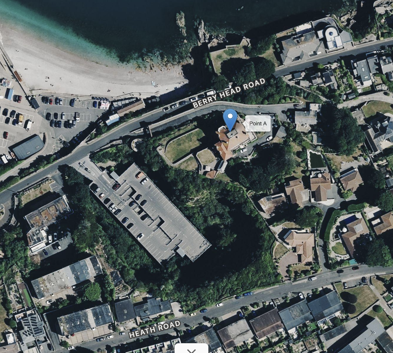 Aerial view of a coastal neighborhood showing a beach, parking lots, residential houses, and streets with a label for Berry Head Road and Heath Road.
