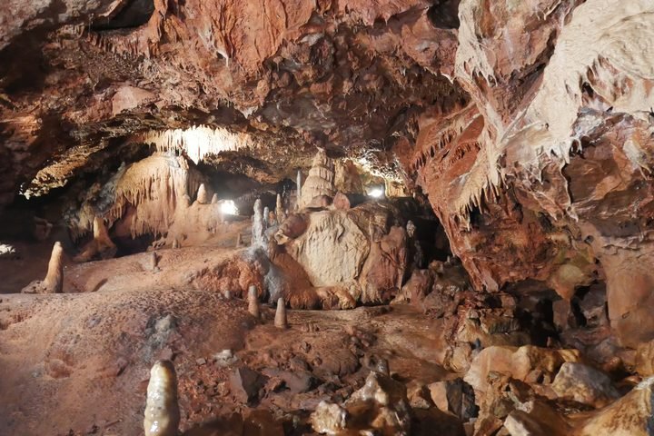 Inside a cave with stalactites and stalagmites, illuminated by artificial lights.